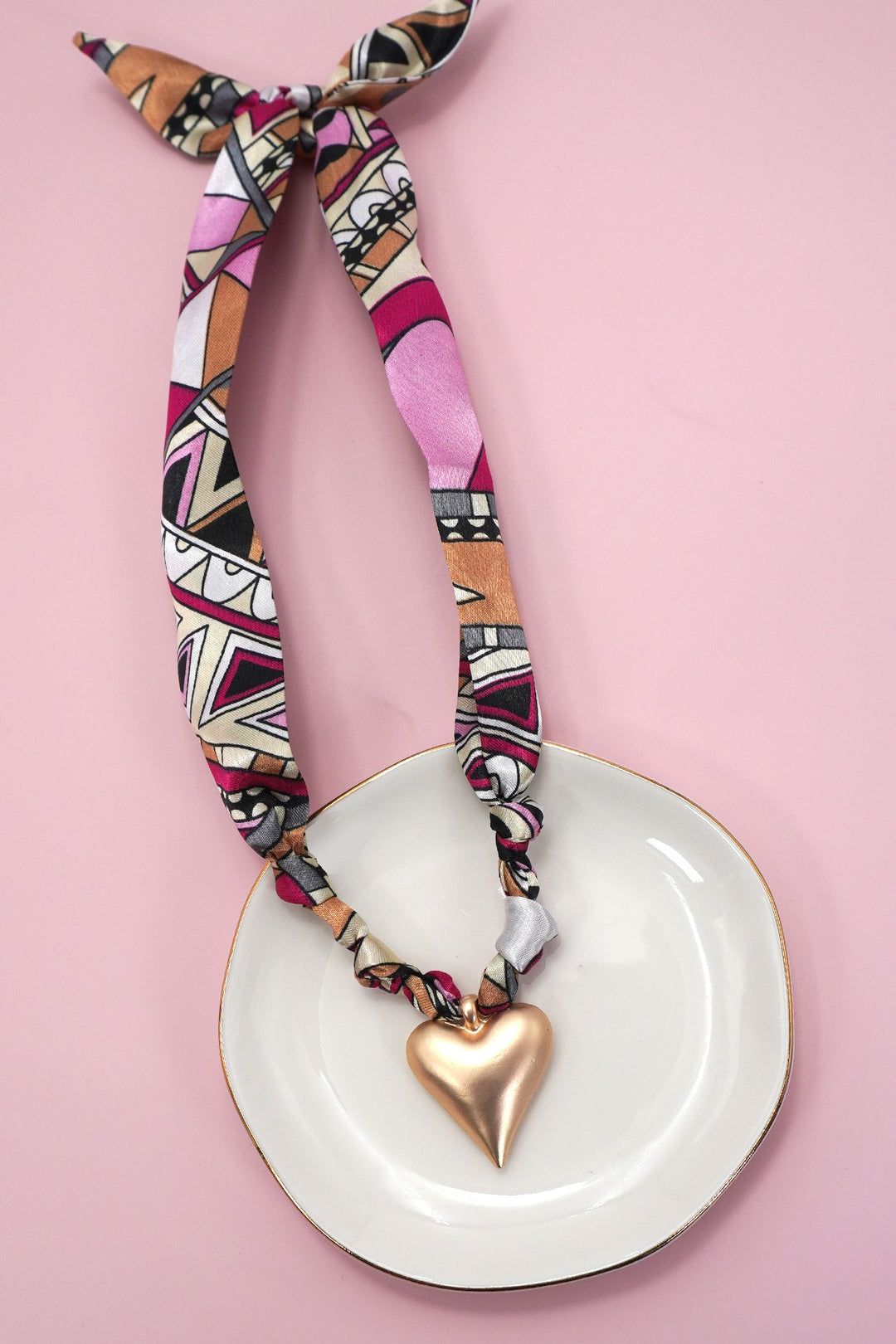 Necklace with a heart pendant on a white plate against a pink background