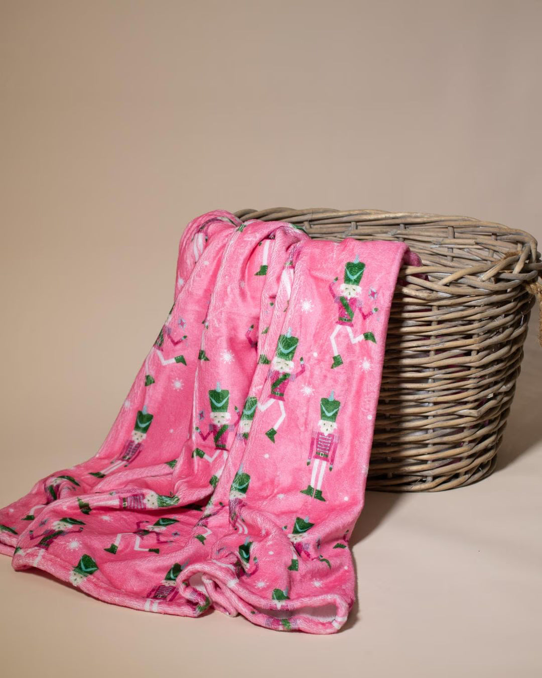 Pink and green nutcracker patterned throw draped over a wicker basket 