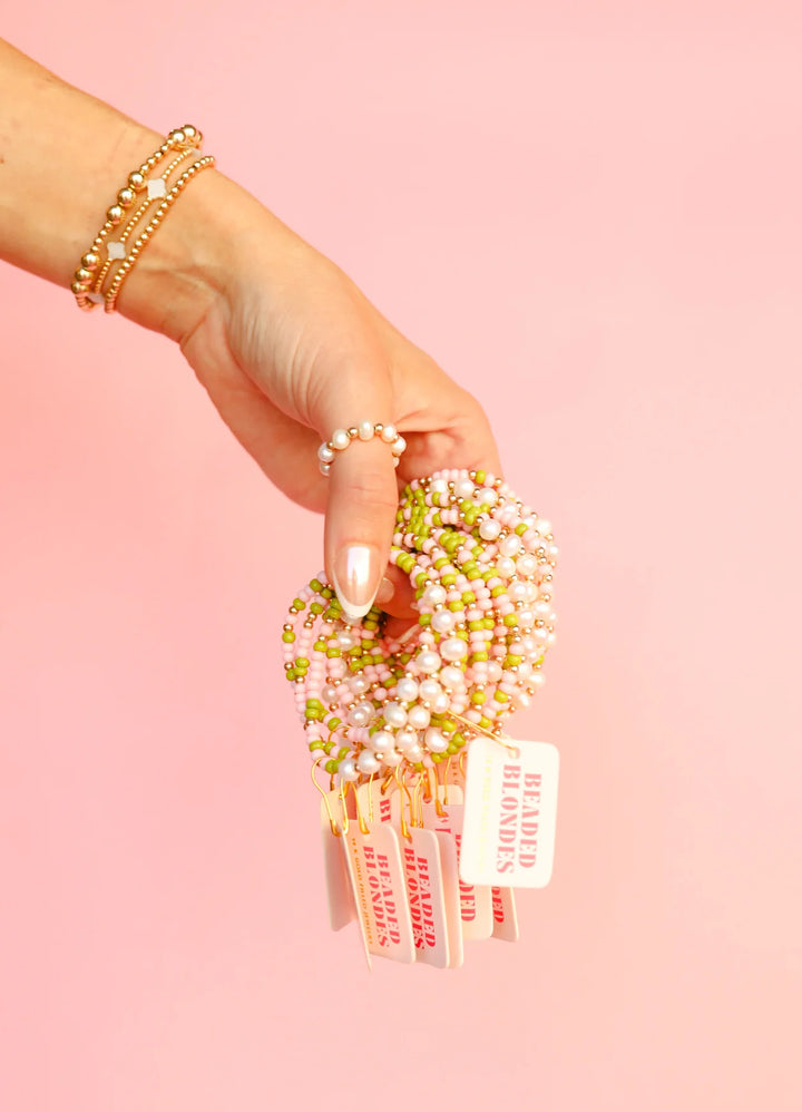 Person holding a set of beaded blonde bracelets with a pink background