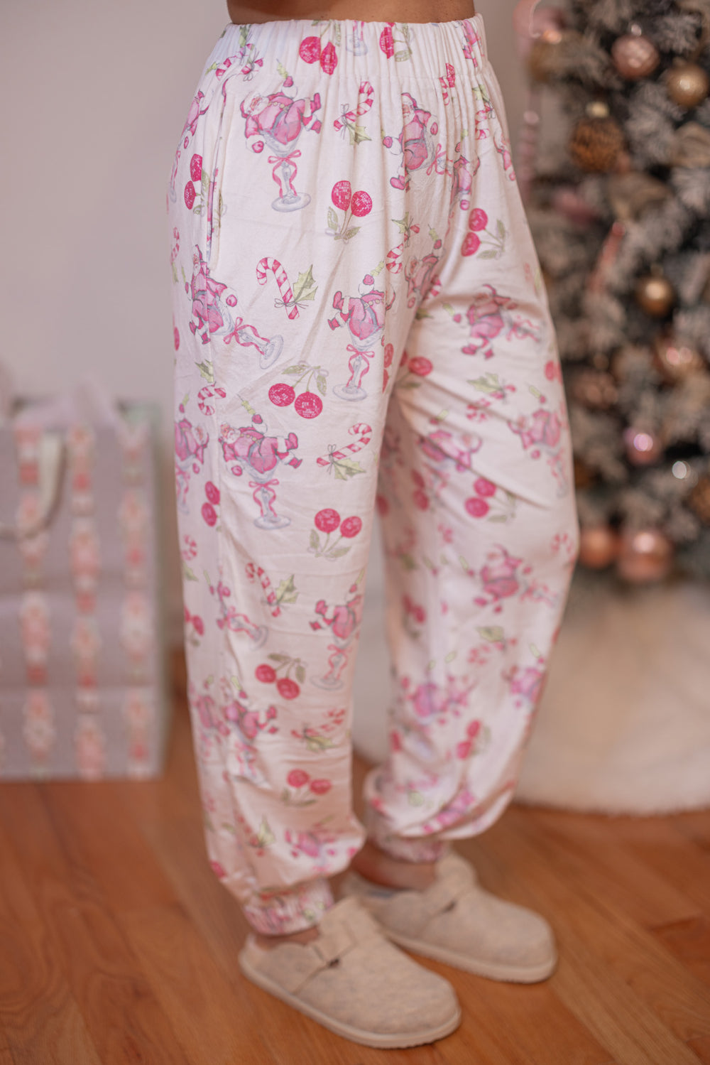 Women's white pajama lounge jogger pants with pink cherry santa print by Peach Love California showing slight side view