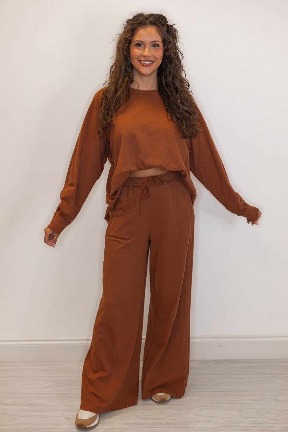 Women's chestnut brown athleisure long sleeve tee and pants set shown with a front tuck and sneakers