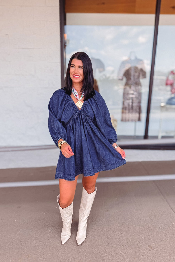 Woman wearing a blue dress and white boots standing in front of a store window.