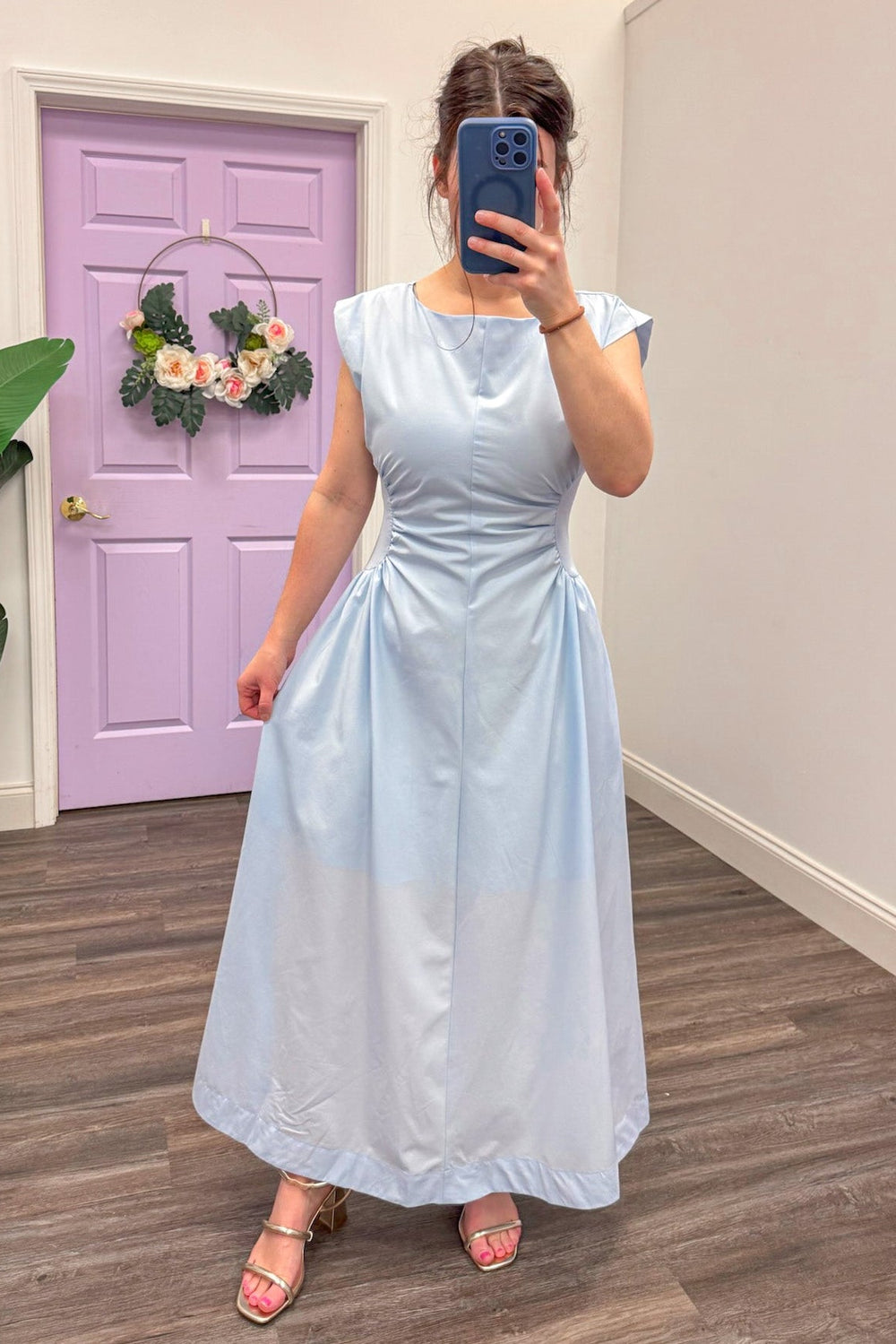 Women's light blue cinched panel waist midi dress paired with gold sandals