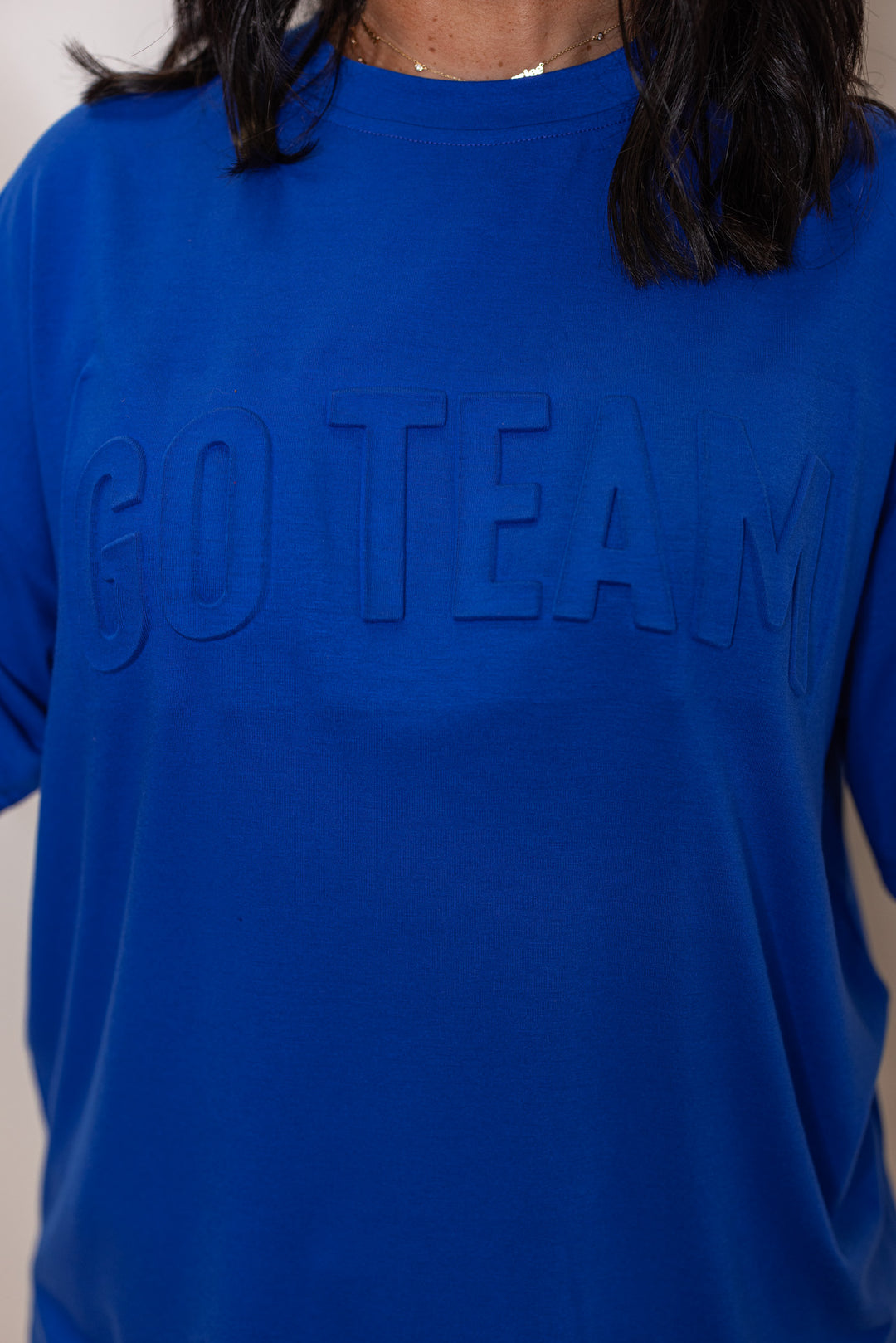 Women's royal blue lightweight top with embossed 'Go Team' in center by Jess Lea showing up close view of embossed lettering